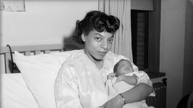 A black and white photo of a Black woman holding a newborn baby in a hospital ed