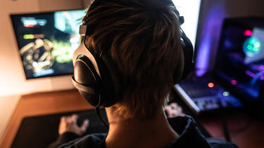 A young man wearing a headset playing a video game, seen from behind
