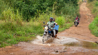 A motorcycle carrying vaccine supplies along a dirt road
