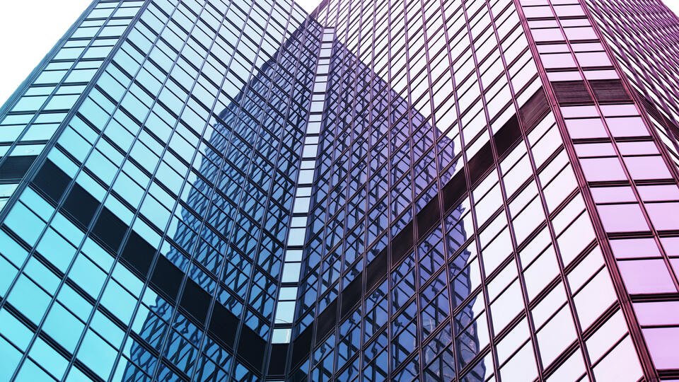 A photo of two wings of a modern glass building appearing to converge
