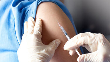 Gloved hands preparing to make an injection into a person's shoulder