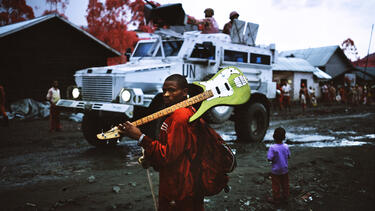 A Congolese musician in the town of Mweso watches as a convoy of United Nations peacekeeping troops, escorted by attack helicopters, withdraws from their camp at Pinga to reinforce other regions.