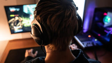 A young man wearing a headset playing a video game, seen from behind