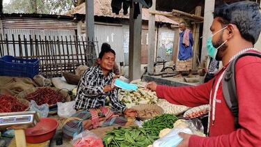 A staff member handing a mask to a vegetable seller in Bangladesh