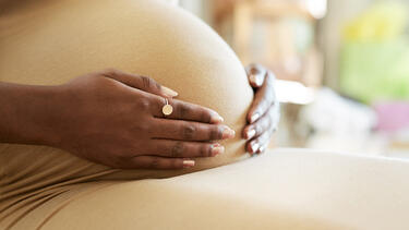 A woman with dark skin holding her pregnant belly