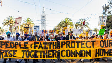 Clergy marching with a banner reading "People of Faith Rise Together to Protect Our Common Home"
