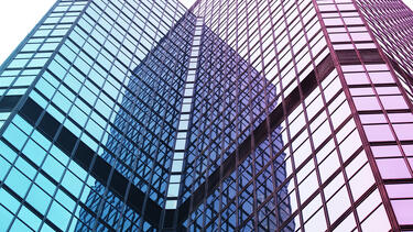 A photo of two wings of a modern glass building appearing to converge