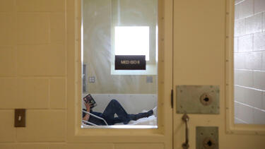 A patient in a prison infirmary, seen through a window