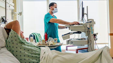 A patient in a hospital bed with a nurse looking at a rolling monitor