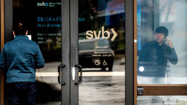 A man reads a notice on the door of Silicon Valley Bank while someone talks on a cell phone inside.