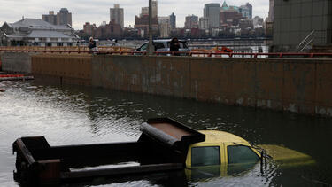 A truck submerged in water with the Manhattan skyline in the background