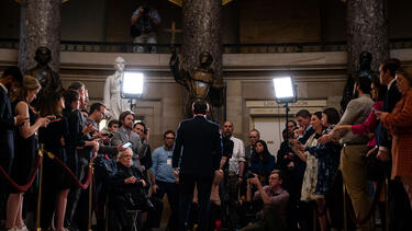 House Speaker Mike Johnson speaking to the press, in a wide image from behind