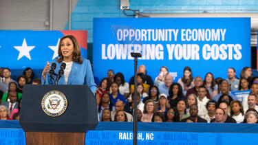 Kamala Harris speaks in front of a banner reading "Opportunity Economy/Lowering Your Costs."