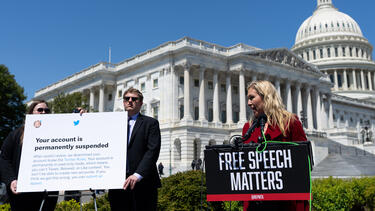 Representative Marjorie Taylor Greene holding a press conference on free speech and Twitter outside the Capitol in April 2022. One poster reads “Free Speech Matters.” Another is of a screenshot from Twitter reading “Your account is permanently suspended.”