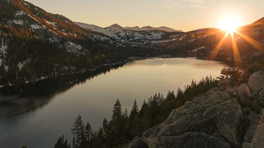 The sun rising over mountains and a lake