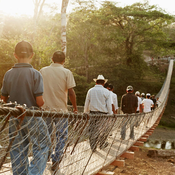 People walking across a suspension footbridge in a rural area