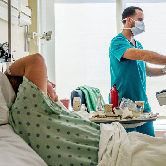 A patient in a hospital bed with a nurse looking at a rolling monitor