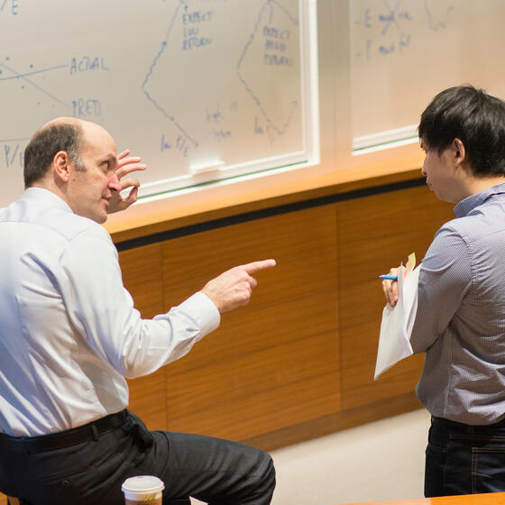 A professor talking with two students in from of a white board