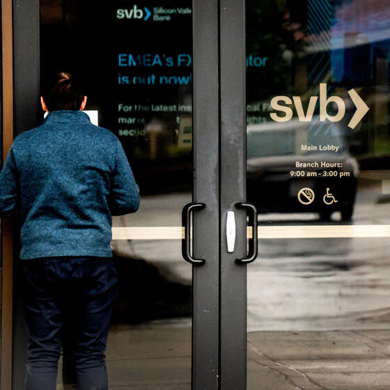 A man reads a notice on the door of Silicon Valley Bank while someone talks on a cell phone inside.