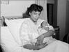 A black and white photo of a Black woman holding a newborn baby in a hospital ed